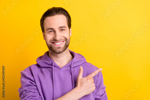 Photo of positive reliable guy direct finger empty space wear violet hoodie isolated yellow color background