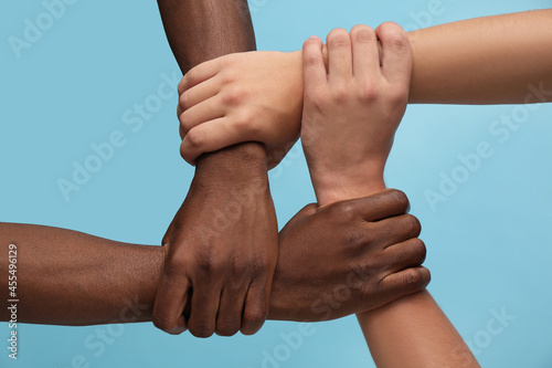 Schilderij op canvas Men joining hands together on light blue background, closeup