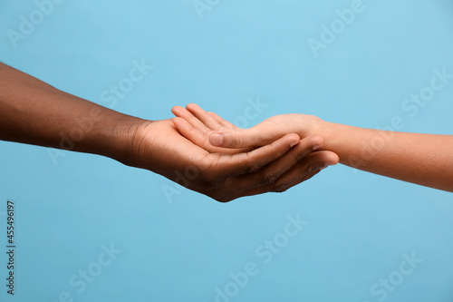 Woman and African American man holding hands on light blue background, closeup