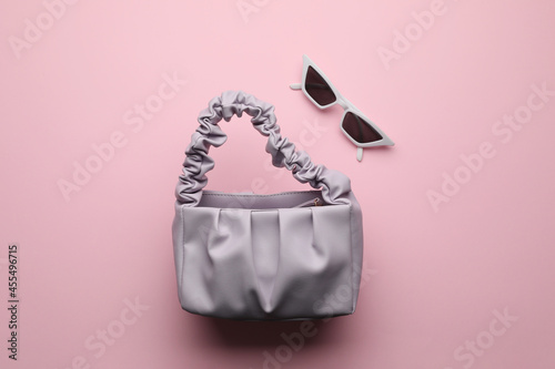 Stylish woman's bag and sunglasses on pink background, flat lay