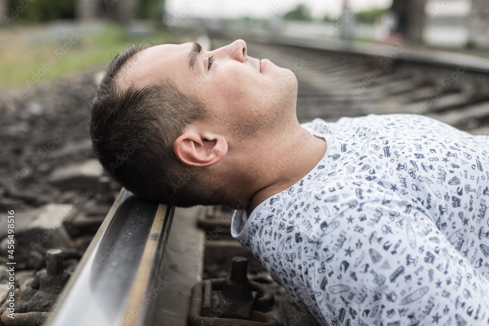A young lonely man is lying on the rails. The head of a man in close-up on the railway tracks. The concept is tragedy, suicide, depression, loneliness. A young lonely man is lying on the rails. The head of a man in close-up on the railway tracks. The concept is tragedy, suicide, depression, loneliness.