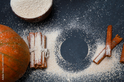 Fresh orange pumpkin, cinnamon, flour scattered from bowl on black table top view. Autumn food, fall homemade cooking concept. Home kitchen, thanksgiving, close up, circular copy space