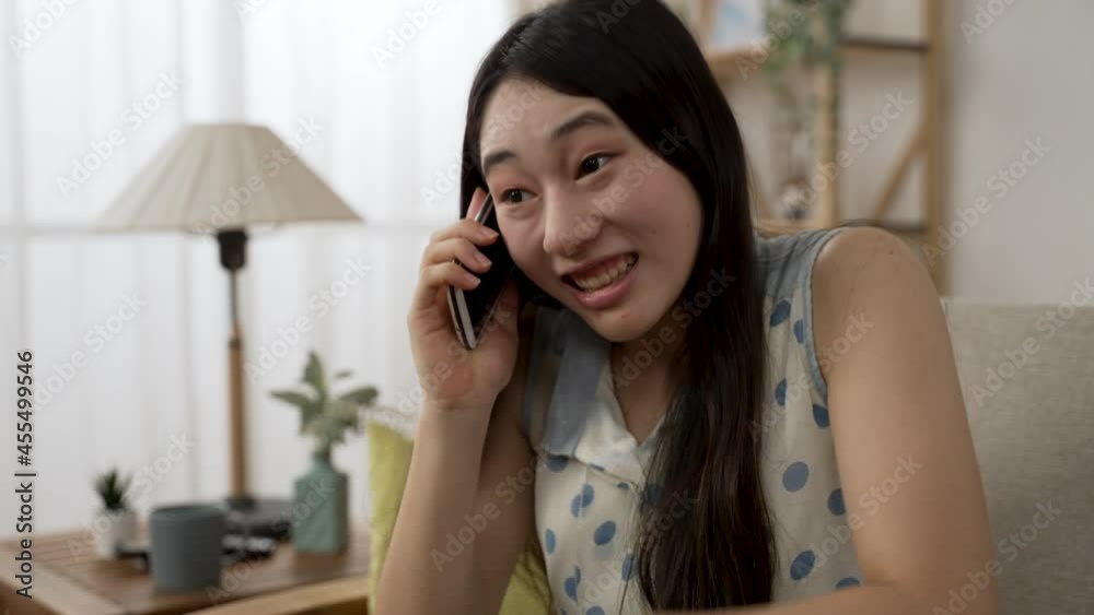 closeup shot of an excited Asian young woman chatting with a smiling face on the smartphone in the living room at home during daytime. closeup shot of an excited Asian young woman chatting with a smiling face on the smartphone in the living room at home during daytime.