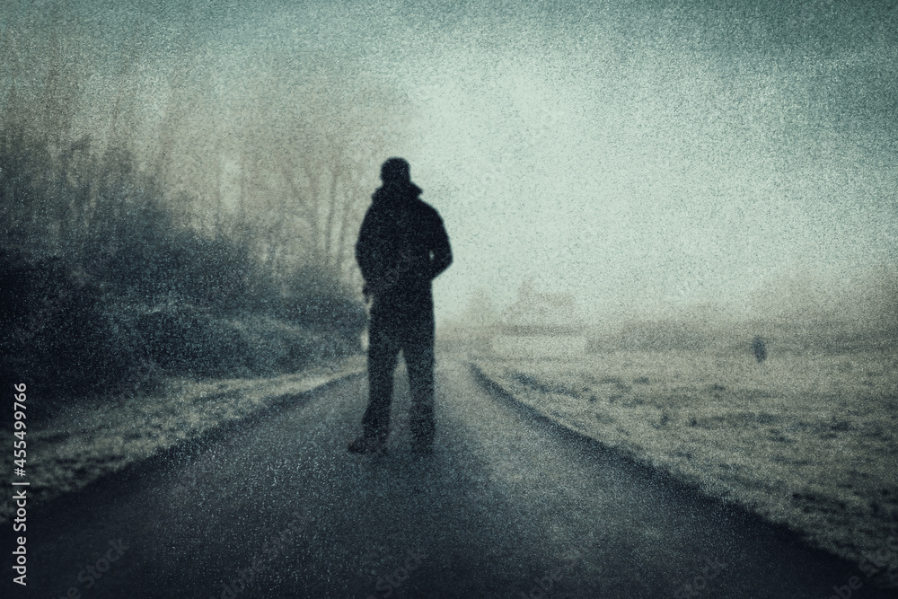A mysterious figure standing on a road in the countryside. On an atmospheric winters day. With a grunge, textured edit. A mysterious figure standing on a road in the countryside. On an atmospheric winters day. With a grunge, textured edit.