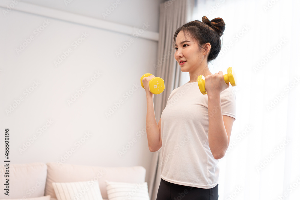 Productive activity concept a girl with a bun wearing a white t-shirt raising the yellow dumbbell with her right hand in her living space