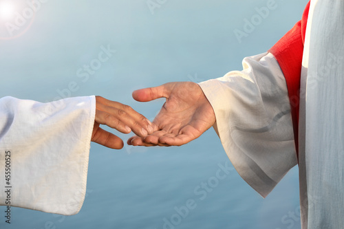 Obraz na plátne Man reaching for Jesus Christ's hand near water outdoors, closeup