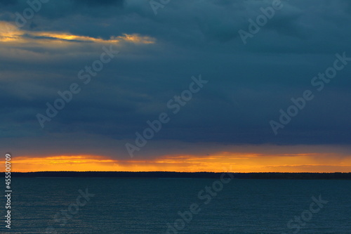 Sunset over the lake with sunlight shining through a cloud in the blue sky.Bright orange stripe on the horizon line.HDR shooting mode