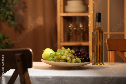 Bottle of wine and plate with ripe fruits on table indoors