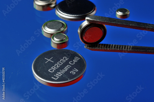 a small battery clamped with tweezers against the background of other small batteries. close-up.