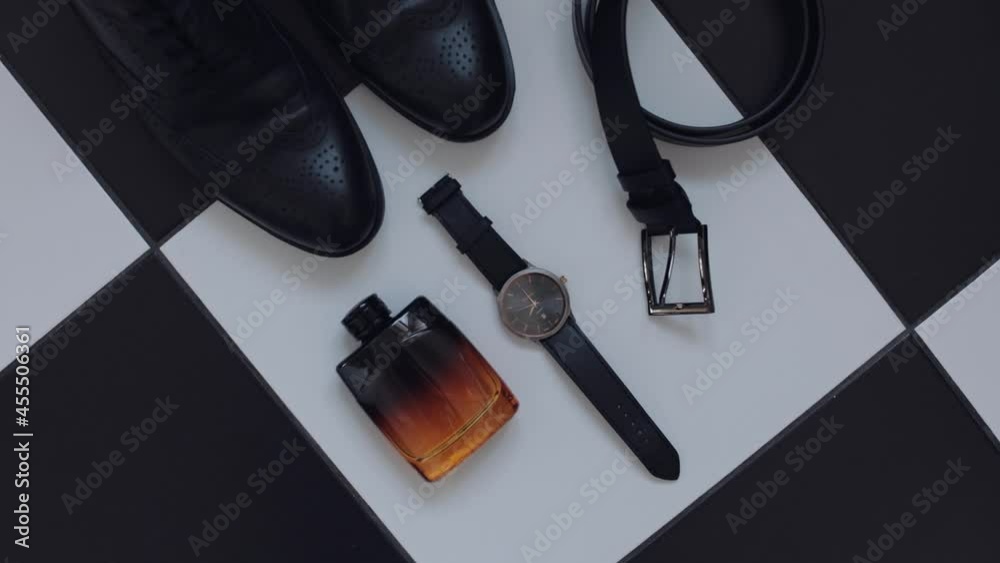 Wedding details of groom. Wedding bridegrooms perfume, belt, shoes and hand clock watch isolated lie on black and white tiles surface. Clothes for a handsome businessman groom. Slow motion footage Wedding details of groom. Wedding bridegrooms perfume, belt, shoes and hand clock watch isolated lie on black and white tiles surface. Clothes for a handsome businessman groom. Slow motion footage