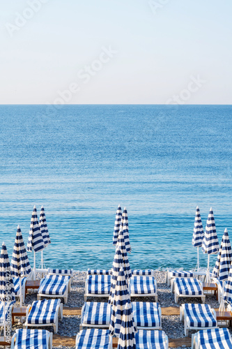 Striped white and blue colored beach chairs with umbrellas lined up on the beach