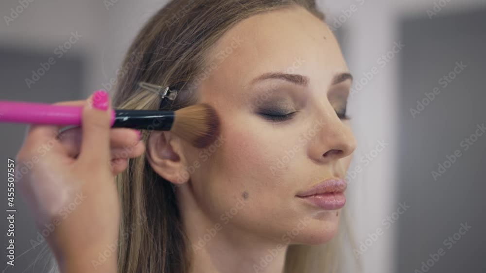 The make-up artist applies the powder on the surface of the young blonde's face The make-up artist applies the powder on the surface of the young blonde's face
