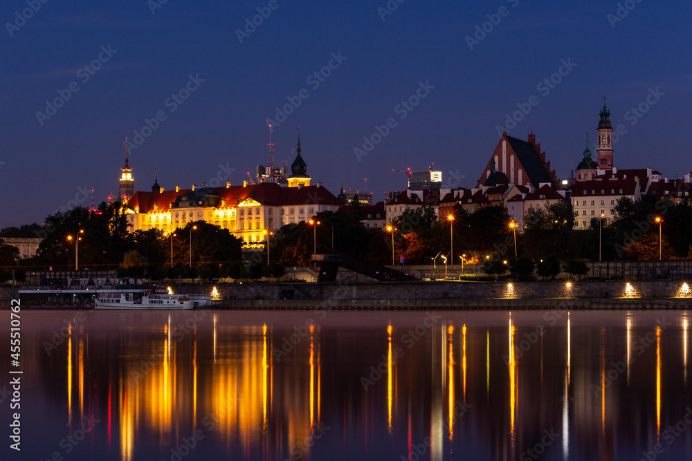 Illuminated Warsaw Old Town landscape with the Royal Castle, Cathedral and medieval buildings, night view with reflections in calm Vistula river, Poland.