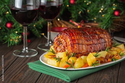 Baked veal roulade with potato and rosemary. Red wine glasses. Christmas holiday dinner on a dark wooden table with a Christmas tree and New Year's toys. photo