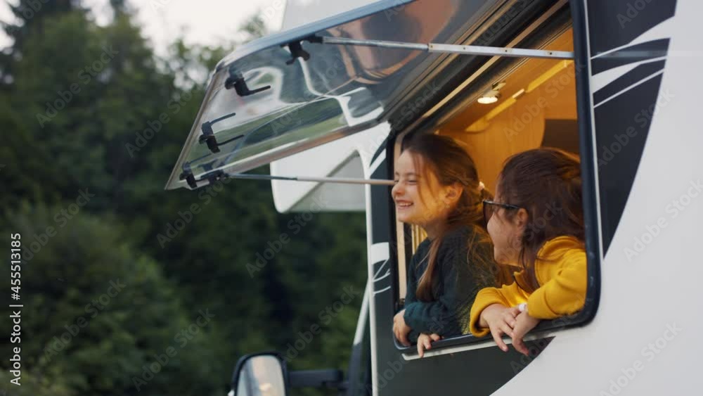 Happy small girls looking out through caravan window in the evening, family holiday trip.