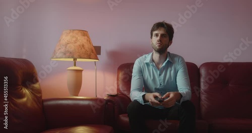 Giovane ragazzo con camicia azzurra guarda la tv seduto nel divano di casa photo