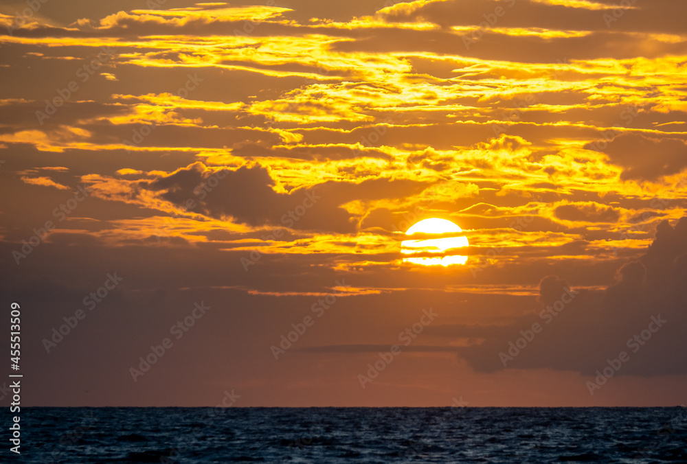 Orange yellow sky with clouds and sun near sunset over the Gulf of Mexico in Southwestern Florida USA