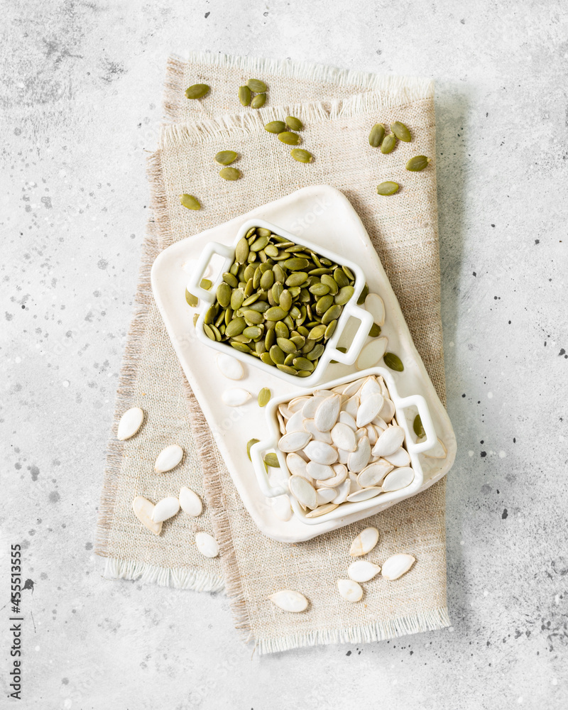 Pumpkin seeds in a white bowl on a light gray culinary background top view