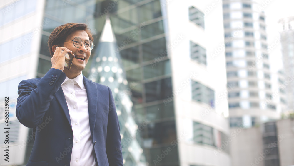Asian businessman using mobile phone app texting outside the office building Asian businessman using mobile phone app texting outside the office building