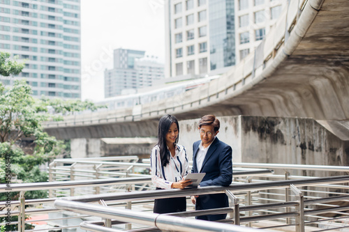 Asian business man and young beautiful woman working on digital tablet computer standing outside office building.