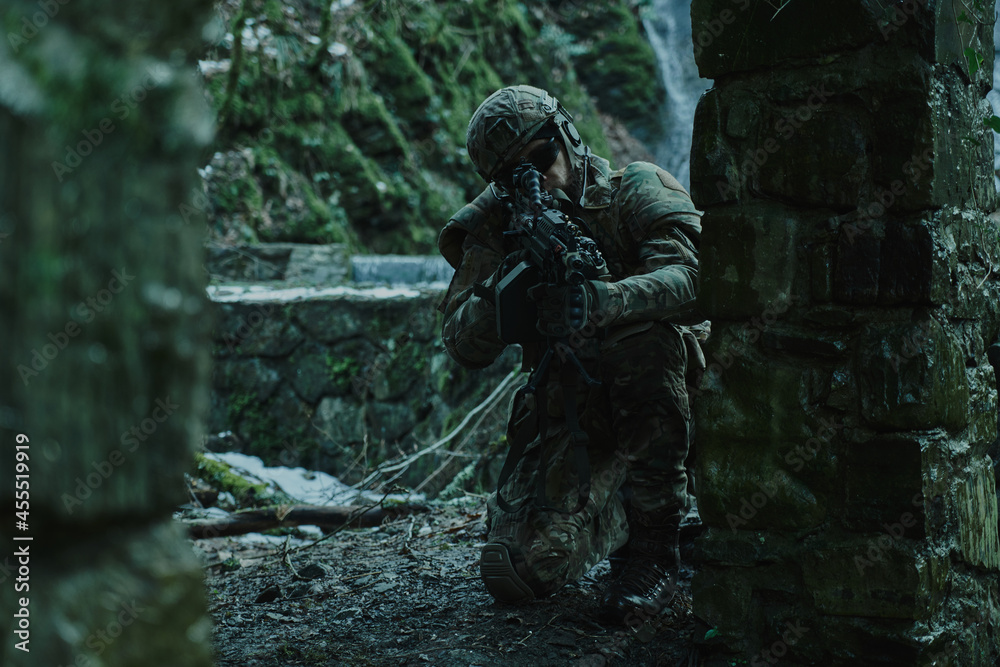 Portrait of airsoft player in professional equipment in helmet aiming at victim with gun in the forest. Soldier with weapons at war Portrait of airsoft player in professional equipment in helmet aiming at victim with gun in the forest. Soldier with weapons at war