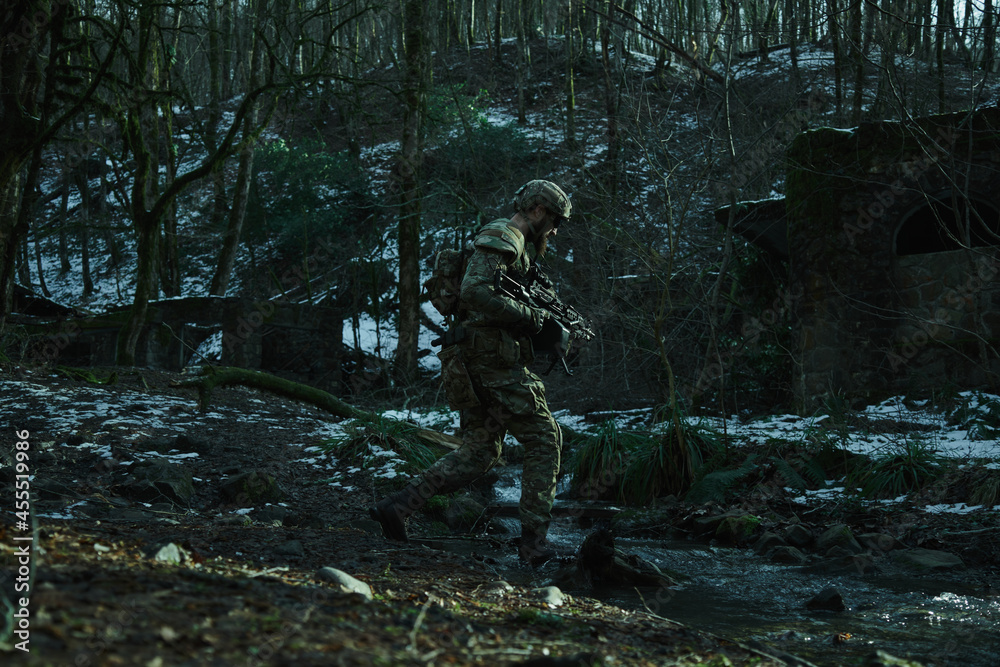 Obraz premium Portrait of airsoft player in professional equipment with machine gun in the forest. Soldier with weapons at war