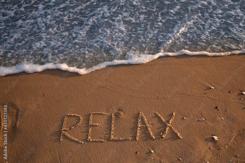 Fototapeta premium Sea wave rolling onto sandy beach with written word Relax, above view