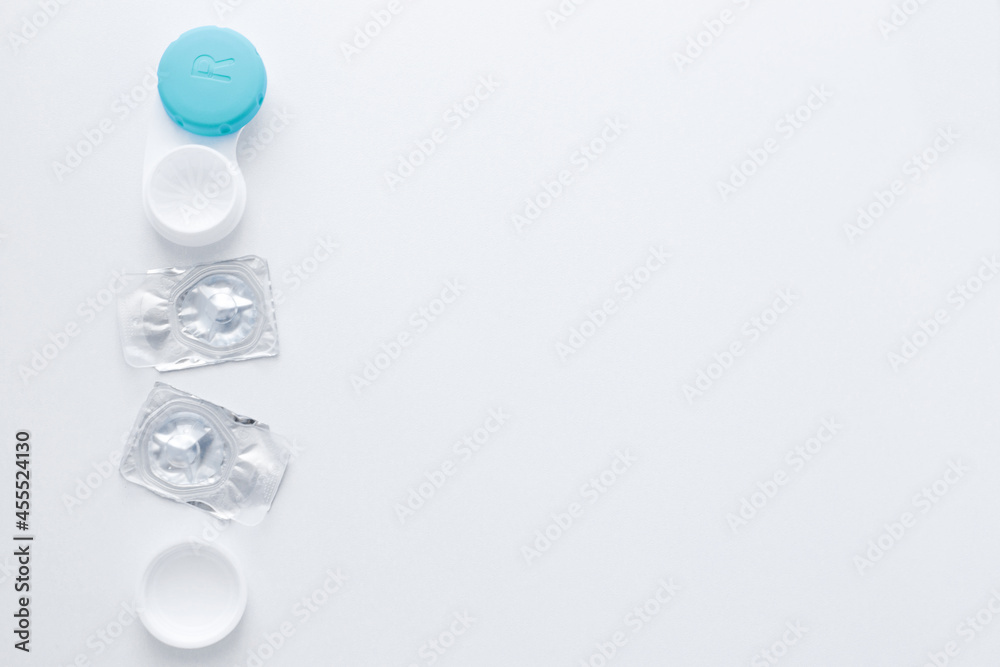 A container for lenses and two sealed lenses lie on the side on a white background with space for text. top view, flat lay, copy space, isolate A container for lenses and two sealed lenses lie on the side on a white background with space for text. top view, flat lay, copy space, isolate