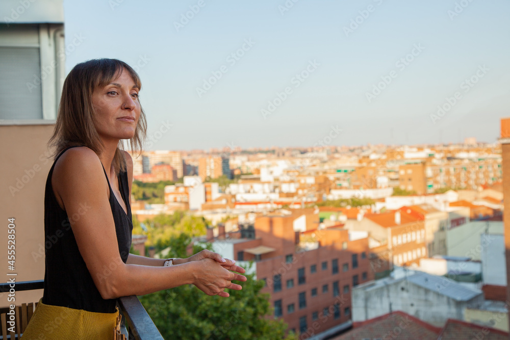 Mujer mirando asomada a su terraza con edificios de fondo. Madrid desde el cielo. Mujer observando la calle. Chica pensando.