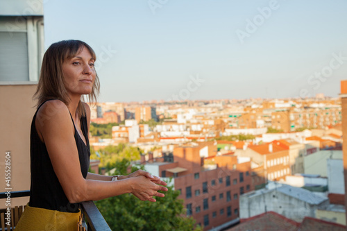 Mujer mirando asomada a su terraza con edificios de fondo. Madrid desde el cielo. Mujer observando la calle. Chica pensando.