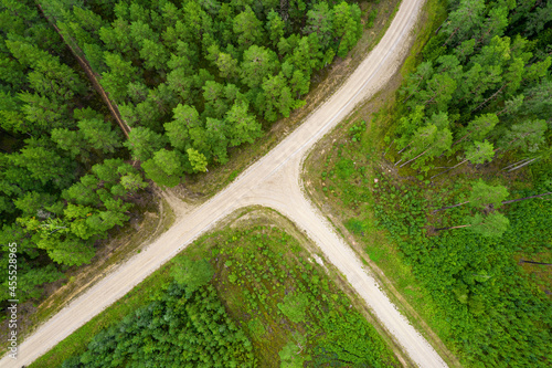 Aerial full frame view from drone of idyllic country intersecting roads in crossroad leading through gallant pine and birch forests in dark green colors in cloudy rainy weather 