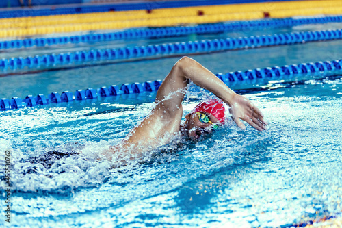 Professional male swimmer in swimming cap and goggles in motion and action during training at pool, indoors. Healthy lifestyle, power, energy, sports movement concept