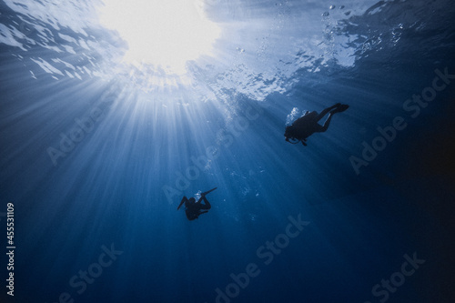 Scuba Divers swimming in to the blue crystal water under sunlights 