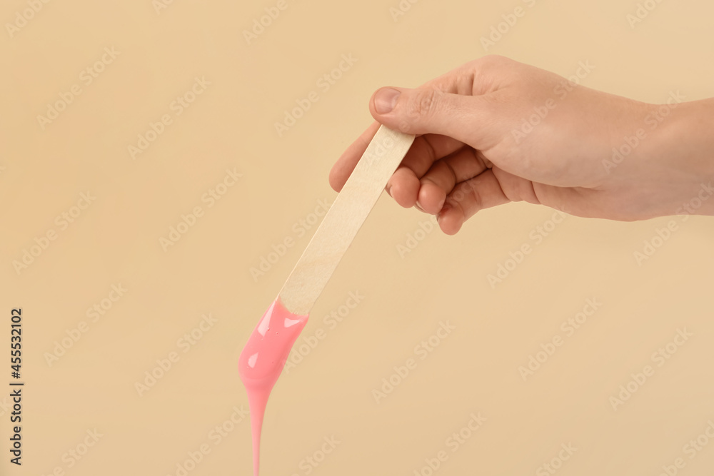 Woman holding spatula with hot depilatory wax on beige background, closeup Woman holding spatula with hot depilatory wax on beige background, closeup