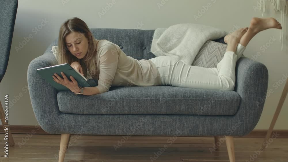Wife planing family budget correcting worksheets on tablet. Student creates personal finance plan. Remote working bussines woman. Housewife controls their spending scroling digital table on couch Wife planing family budget correcting worksheets on tablet. Student creates personal finance plan. Remote working bussines woman. Housewife controls their spending scroling digital table on couch