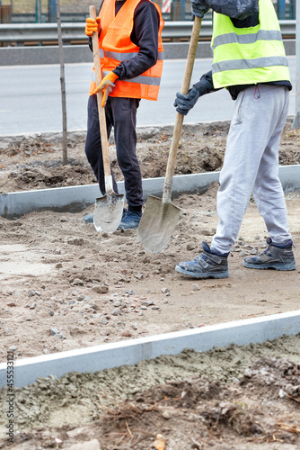 Road workers use shovels to level a sandy foundation on a track under construction on a spring day. Vertical image.