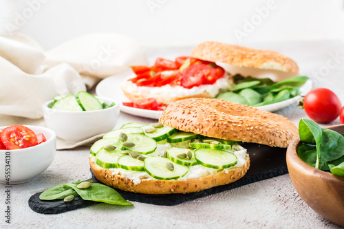 Delicious bagel stuffed with feta, cucumber and pumpkin seeds and spinach leaves on a slate board. Light Vitamin Healthy Snack