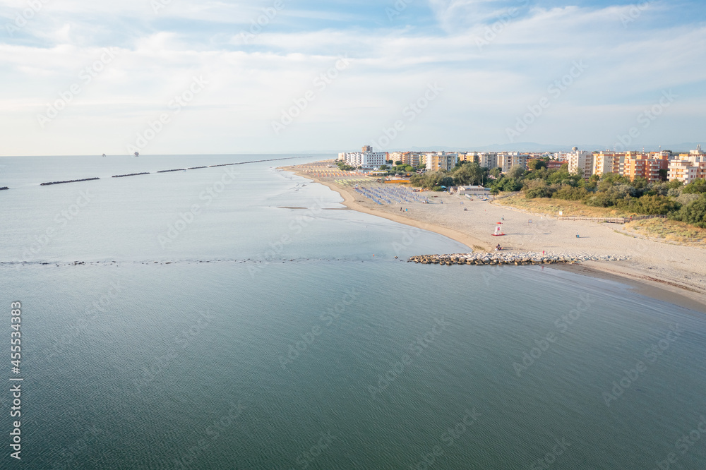 Drone shot of sandy beach with umbrellas,gazebos and town background.Summer vacation concept.Lido Adriano town,Adriatic coast, Emilia Romagna,Italy.