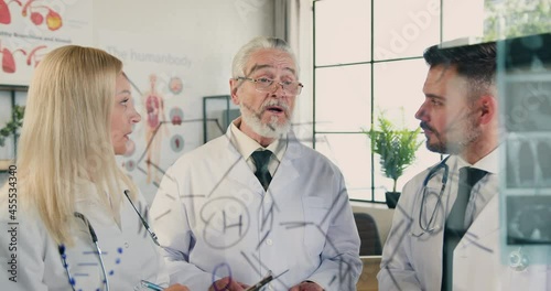 Attractive respected skilled bearded doctor talking to his attantive successful male and female colleagues in medical office near glass wall with results of x-ray scan photo