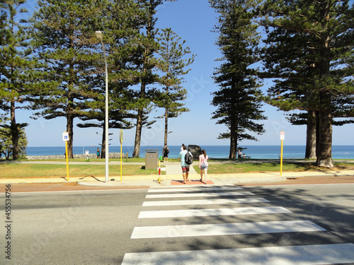 People traversing a crosswalk towards the beach. Pine trees, green grass, blue sea and blue sky. Cottesloe, Australia, 2013. photo