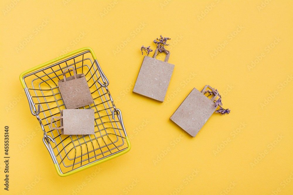 A pair of eco-friendly craft paper bags in and near a metal shopping basket with dried flowers on a yellow background. Black friday gift sales
