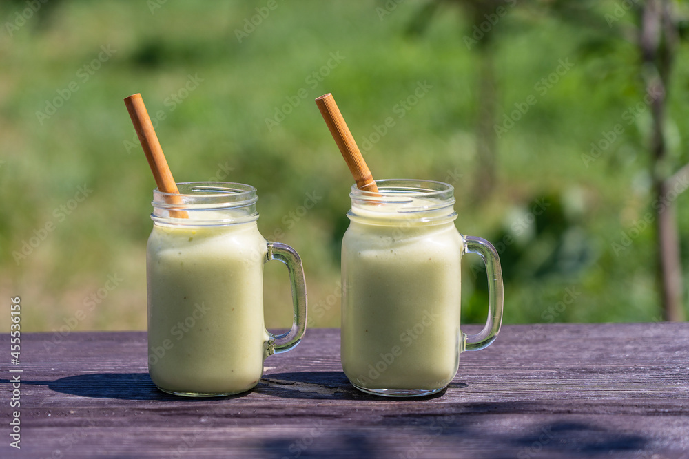 Fresh green smoothie from avocado, banana and honey in glass mug on wooden table in nature background Fresh green smoothie from avocado, banana and honey in glass mug on wooden table in nature background
