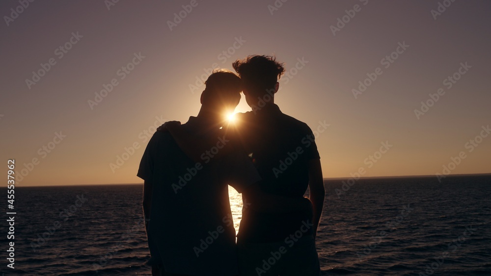 Happy gay couple hugging at sunset near the sea, enjoying time together outdoors