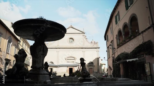 Italian ancient characteristic street with antique building exterior and round fountain with marble statues, catholic Church in the centre of the street with arched door and round stained glass window photo