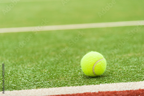 A yellow tennis ball lies on a green artificial tennis court, photo from copy space.