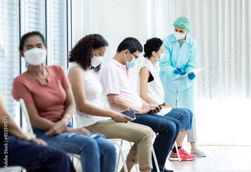 Diverse people lining up waiting sit for their turn to get shots at the hospital vaccination center.