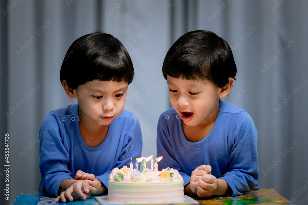 Twins adorable boy in blue shirt, celebrating his birthday, blowing candles on homemade baked cake, indoor. Birthday party for kids Twins adorable boy in blue shirt, celebrating his birthday, blowing candles on homemade baked cake, indoor. Birthday party for kids
