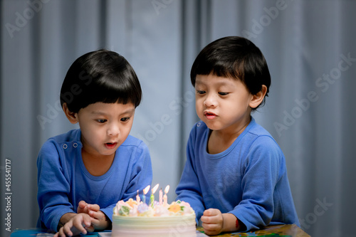 Twins adorable boy in blue shirt, celebrating his birthday, blowing candles on homemade baked cake, indoor. Birthday party for kids