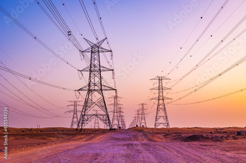 High voltage tower with electricity transmission power lines against the colorful sky, low angle view. Dubai Al Qudra Desert United Arab Emirates.