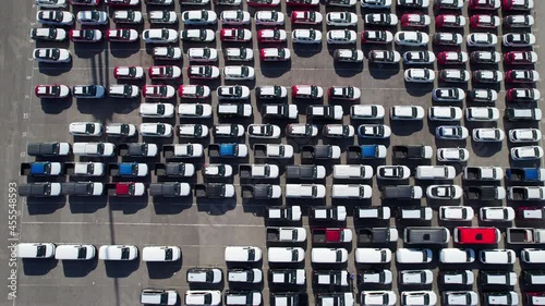 Aerial view large parking lot with new cars for sale in port of large sea city arrived by cargo ship in country drone turn automotive plant. Industrial